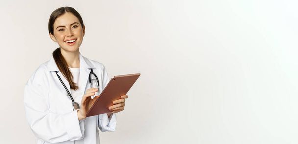 Doctor in white coat using digital tablet, reading medical data on gadget, working in hospital, standing over white background. - Foto, imagen