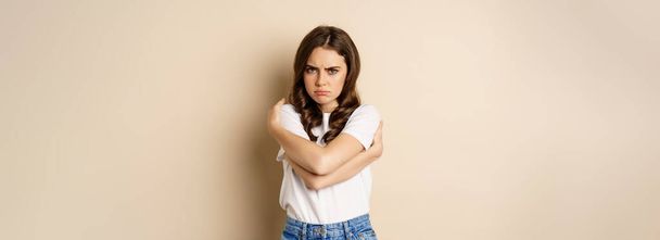 Offended angry woman cross hands on chest, frowning and sulking insulted, standing over beige background. - Fotoğraf, Görsel