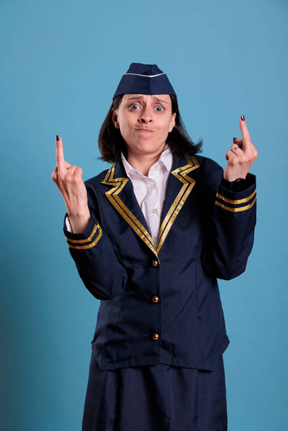 Aggressive furious airplane flight attendant showing middle finger offensive gesture. Angry airline stewardess in professional uniform demonstrating provocative rude behavior - Photo, Image