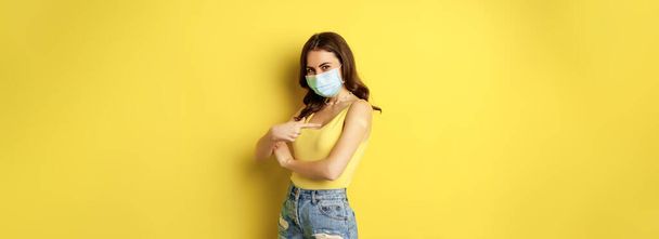 Covid-19 vaccination. Beautiful young woman in face medical mask got vaccinated during pandemic, standing over yellow background. - Foto, Imagem