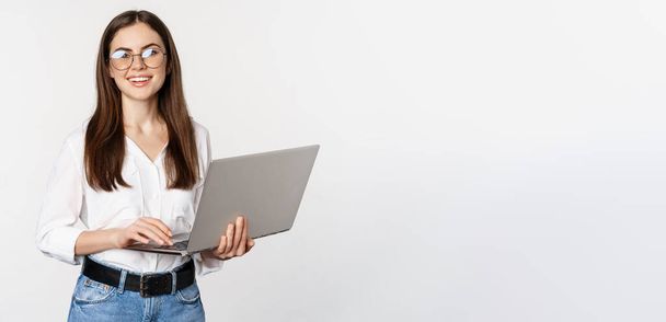 Portrait of young office woman, entrepreneur answer clients on laptop, working with computer with happy face, standing over white background. - Foto, Imagem
