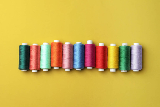 Set of colorful sewing threads on yellow background, flat lay - Photo, image