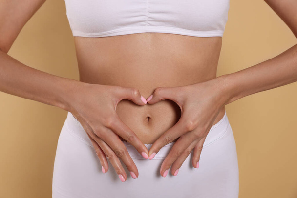 Woman in underwear making heart with hands on her belly against beige background, closeup. Healthy stomach - Foto, afbeelding