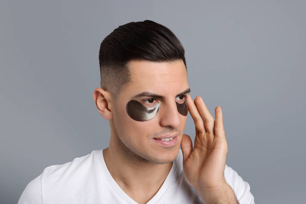 Man applying dark under eye patch on grey background - Fotó, kép