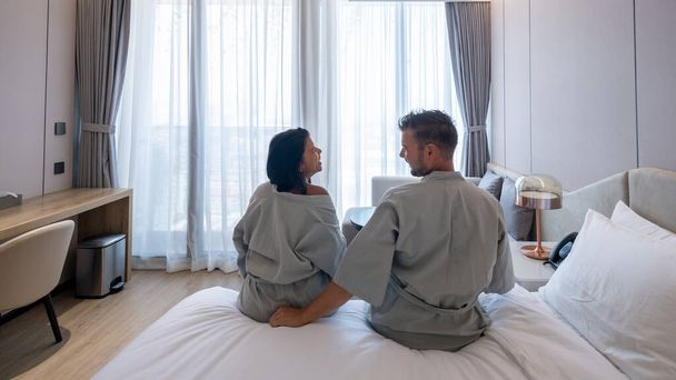 Paar wacht im Hotelzimmer auf, thailändische asiatische Frauen und kaukasische Männer wachen im Bett eines Luxushotels auf. - Foto, Bild
