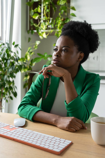 La donna afroamericana premurosa con occhiali in mano guarda attentamente verso computer si siede a tavolo di ufficio con tazza di caffè. Professionale business lady controlla il rapporto dei dipendenti inviato via e-mail - Foto, immagini