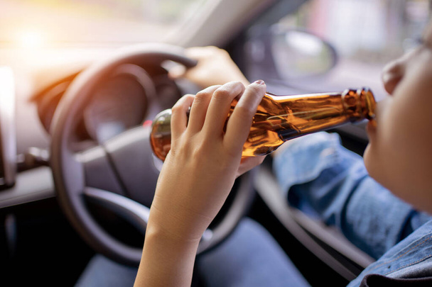 危険な街の夕日の中で運転しながら、アジアの女性はビールを飲む,右側のドライブシステム. - 写真・画像