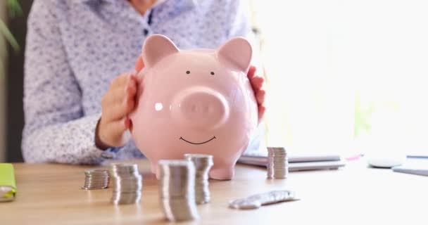Frau hält rosa Sparschwein in der Hand und streicht über finanzielle Ersparnisse. Anhäufung von Anlagevermögen und Geschäft - Filmmaterial, Video