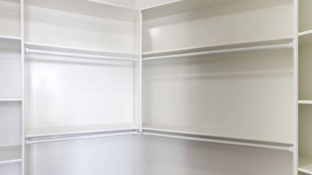 Panorama Blanco construido en la unidad de estantería de montaje en pared en un walk in closet. Walk in closet interior con suelo de moqueta marrón y estantes enmarcados con varillas de plástico debajo. - Foto, Imagen