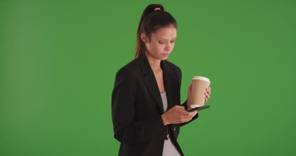 Happy professional woman interacting with cellphone and texting on greenscreen. Charming young business woman holding cup and using smart phone to send text messages standing on green screen. 4k - Footage, Video