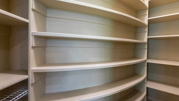 Panorama Kitchen pantry interior of a house with wooden shelving unit. Small spaced empty pantry with wall shelves with curved and edged structures and a steel wire shelves on the right shelf. - Photo, Image
