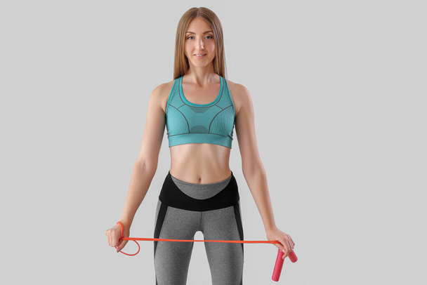 Sporty young woman with jumping rope on light background - Fotografie, Obrázek