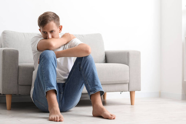 Стрессовый молодой человек сидит дома на полу - Фото, изображение
