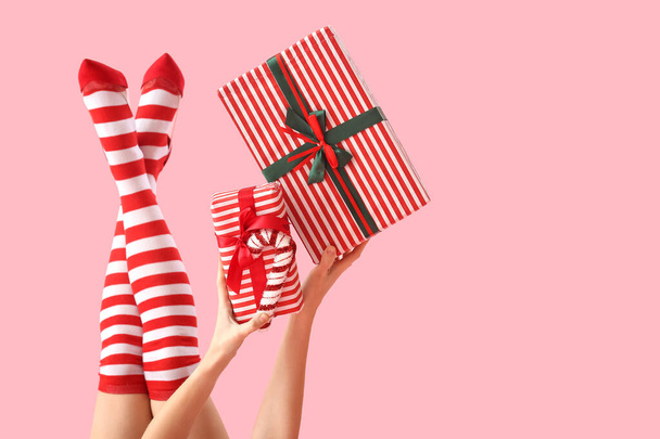 Mujer en medias de Navidad con cajas de regalo sobre fondo rosa - Foto, imagen