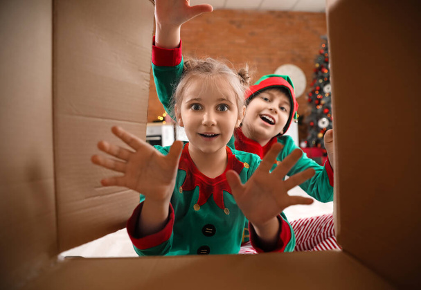 Niños pequeños vestidos como elfos con caja de regalo de Navidad abierta en la cocina, vista desde el interior - Foto, imagen