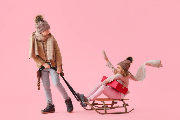 Kis gyerekek szánkó és karácsonyi ajándék rózsaszín háttér - Fotó, kép