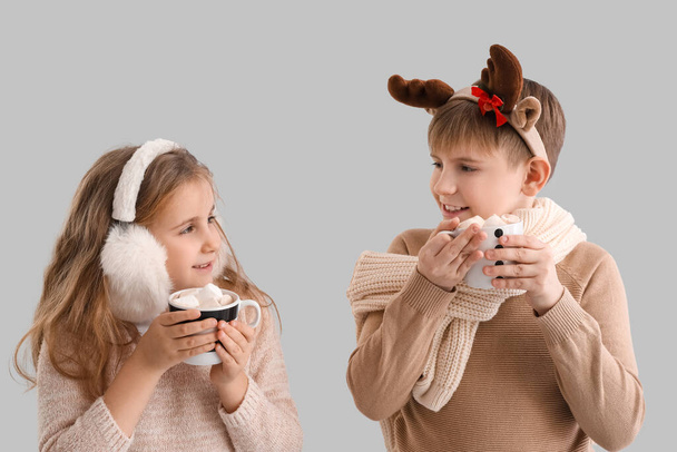 Niños pequeños con tazas de cacao sobre fondo gris - Foto, imagen