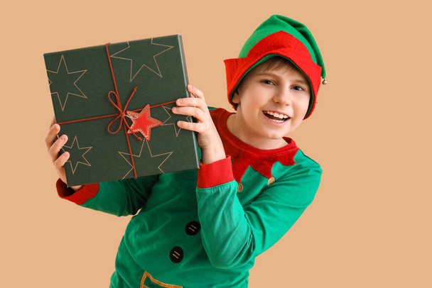 Little boy dressed as elf with Christmas gift on beige background - 写真・画像
