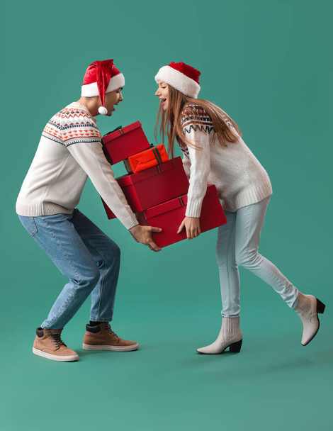 Happy young couple in Santa hats with Christmas presents on green background - Photo, Image