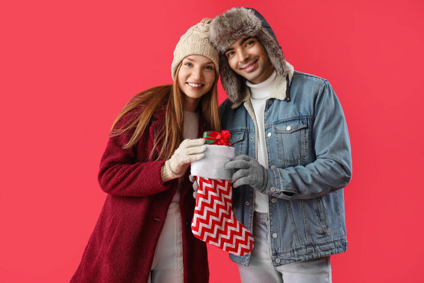 Счастливая молодая пара с рождественским носком и подарком на красном фоне - Фото, изображение