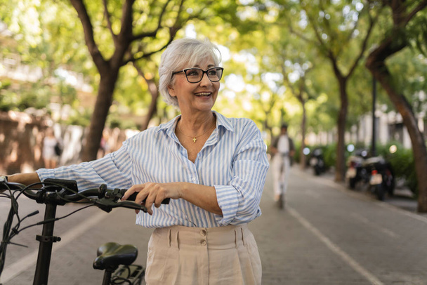 Happy gray hair mature woman mature walking with bicycle in the city - Foto, afbeelding
