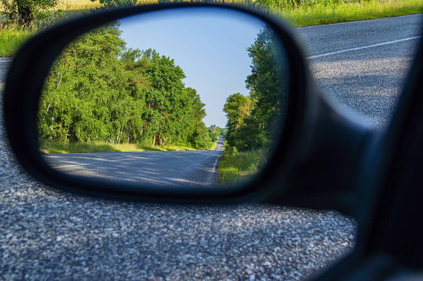 Reflexión en el espejo de un coche de una carretera asfaltada de dos carriles con marcas blancas. Reflejo en el espejo del coche. Asfalto pavimento. Lugar para el tráfico de coches. Autoturismo y viajes. La belleza. - Foto, Imagen
