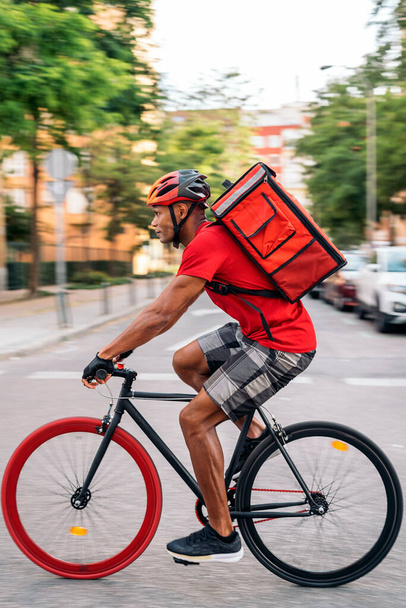 African delivery man wearing safety helmet riding his bike in the city in his way to deliver a package. - 写真・画像