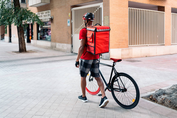 彼のクールな自転車で街を歩く認識されていないアフリカの配達人. - 写真・画像