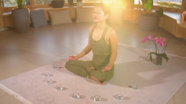 Lassú mozgás: meditáló gyönyörű ázsiai nő pihentető otthoni környezetben. Iszapot termel, hogy stimulálja az életerő áramlását. Női személy fokozza az életenergia, míg a meditáció lótuszban pózol - Felvétel, videó