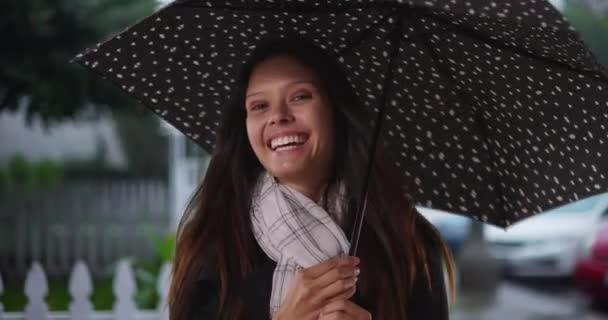 Joyeux parapluie millénaire femelle tournant devant sa maison dans la tempête de pluie. Femme blanche dans la vingtaine avec parapluie à pois dans la rue du quartier avec des voitures souriantes. 4k - Séquence, vidéo