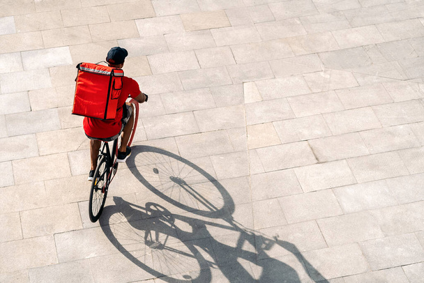 Африканський доставник в кашкеті їздить на велосипеді в місті, щоб доставити пакет. - Фото, зображення