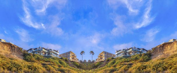 Fond miroir abstrait Vue en angle bas d'une pente de montagne avec des plantes sauvages et des bâtiments sur le dessus à San Clemente, CA. Il y a deux immeubles d'appartements sur la gauche avec balcons contre le ciel - Photo, image