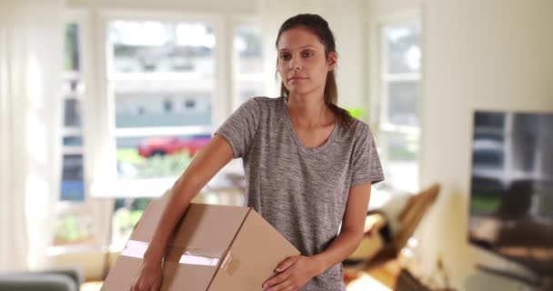 Серьезная молодая женщина в квартире с коробкой для переезда. Женщина въезжает или переезжает, удерживая картонную коробку дома. 4k - Кадры, видео