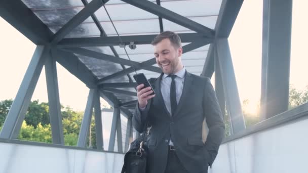  Un hombre de negocios con un traje de negocios habla en una videollamada mientras camina por la calle. Un hombre de negocios estadounidense está chateando video usando un teléfono inteligente. Vídeo 4k - Metraje, vídeo