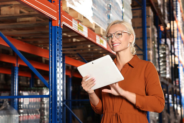 Happy manager using modern tablet in warehouse with lots of products - Foto, imagen