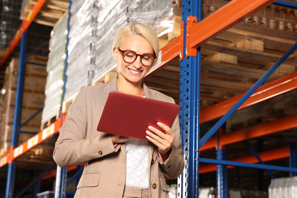 Happy manager using modern tablet in warehouse with lots of products - Foto, Bild