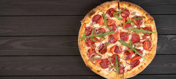 Pizza met ham, rucola en groenten op donkere houten ondergrond. Een spandoek. Ruimte voor uw tekst - Foto, afbeelding