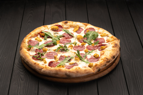 Classic Italian meat pizza with salami, cheese, arugula on a plate. Black background. Italian cuisine, selective focus. Copy pace - Photo, Image