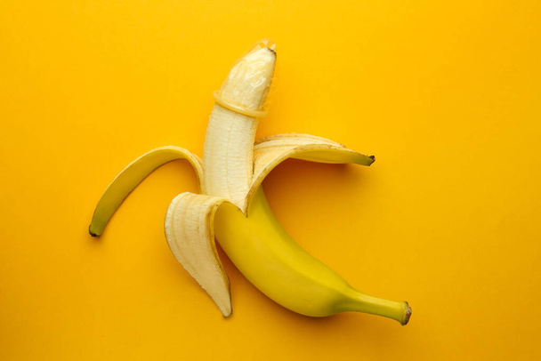 Plátano con condón sobre fondo naranja, vista superior. Concepto de sexo seguro - Foto, imagen