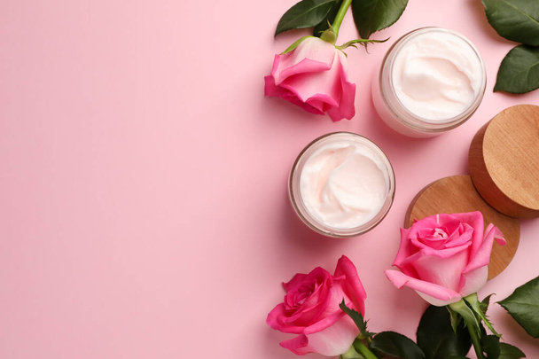 Glass jars of face cream and roses on pink background, flat lay. Space for text - Foto, imagen
