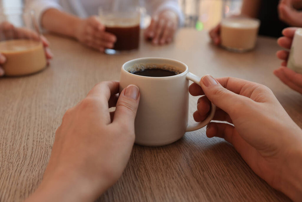 Woman holding cup of coffee spending time with friends in cafe, closeup - Foto, Imagen
