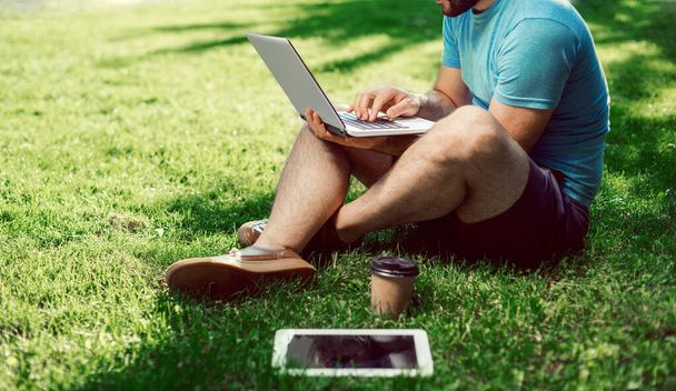 Młody bloger siedzi na trawie i pracuje z laptopem. Przestrzeń kopiowania - Zdjęcie, obraz