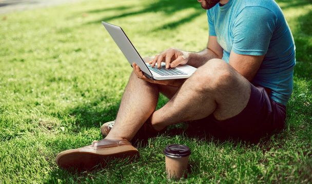 Genç blogcu çimlerde oturuyor ve dizüstü bilgisayarla çalışıyor. Boşluğu kopyala - Fotoğraf, Görsel