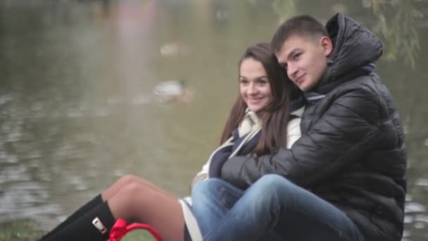 Αγαπώντας ζευγάρι αγκαλιάζει κάθεται κοντά στη λίμνη - Πλάνα, βίντεο