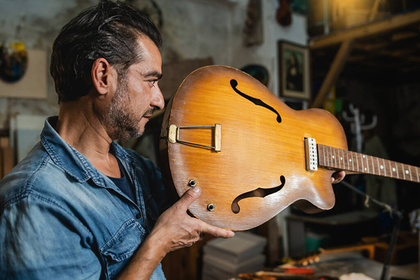 Ένας luthier ελέγχει έναν κοίλο λαιμό κιθάρας σώματος στο εργαστήριό του για να επαληθεύσει την ευθυγράμμιση - άνθρωποι, τέχνες και τέχνη έννοια - Φωτογραφία, εικόνα