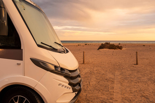Modern camper van motor home in free adventure parking. Concept of renting camping car vehicle for alternative free off grid van life life vacation. Sunset and beach with amazing sky in background - Photo, Image