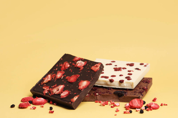 Different chocolate bars with freeze dried fruits on yellow background, space for text - 写真・画像
