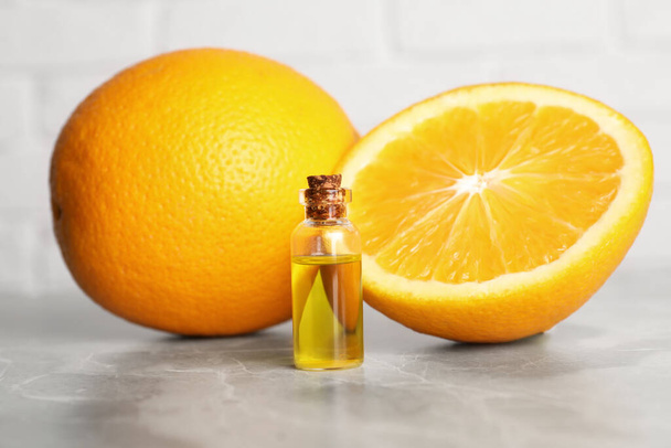 Bottle of essential oil with oranges on grey marble table, closeup - Фото, изображение