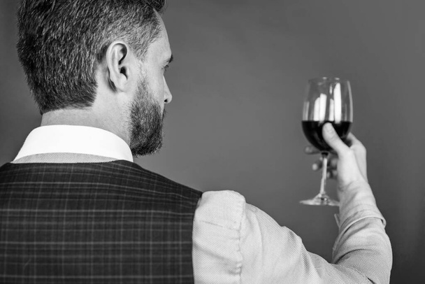 mature man sommelier or bartender tastes glass of red wine, back view selective focus, luxury drink. - 写真・画像