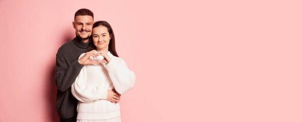 Portrait of lovely young couple, man and woman, making heart shape with hands, posing isolated over pink background. Concept of love, relationship, Valentines Day, emotions, lifestyle, holiday. Flyer - Photo, Image